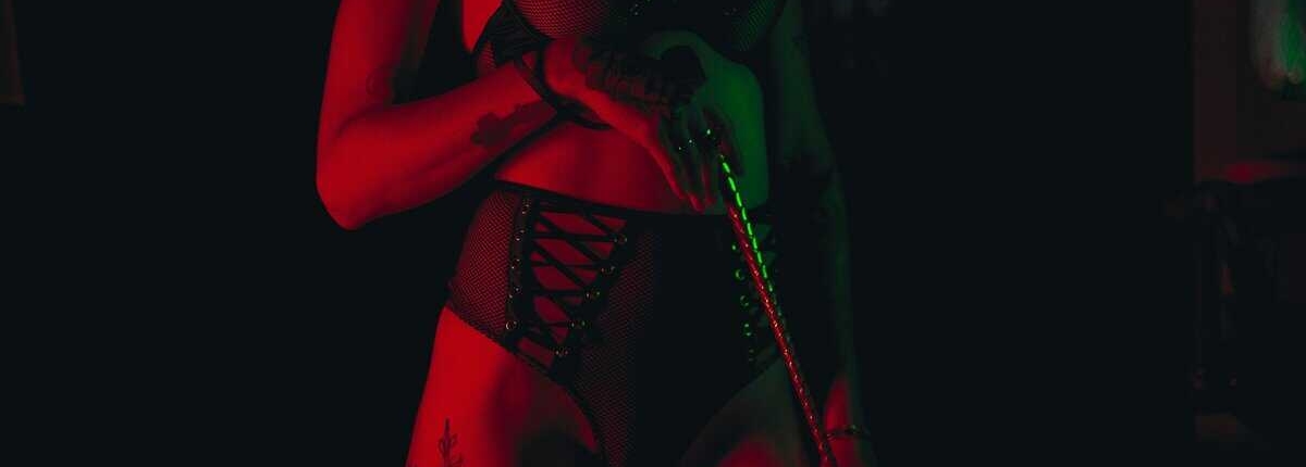 Mulher em pé segurando um chicote em um cenário de sadismo