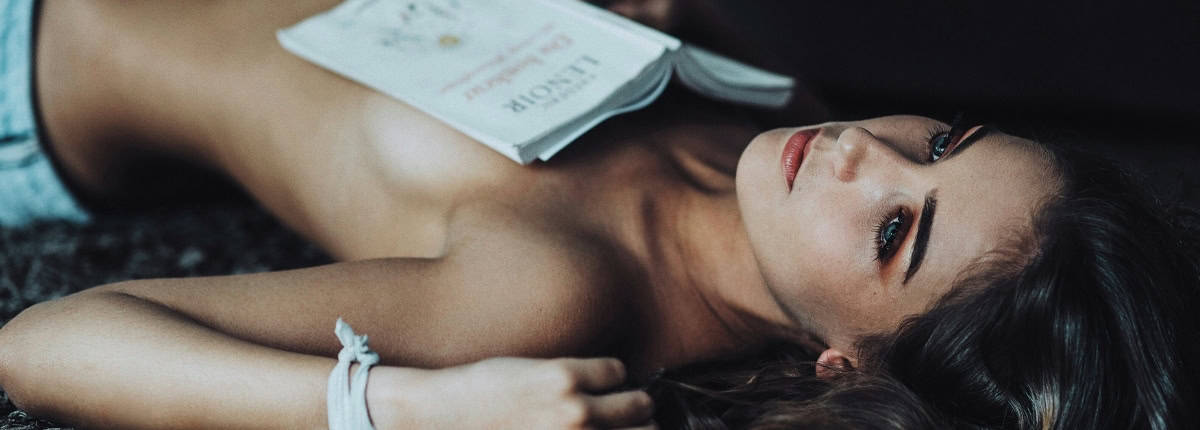 Mulher deitada no chao com um livro de Contos Eróticos