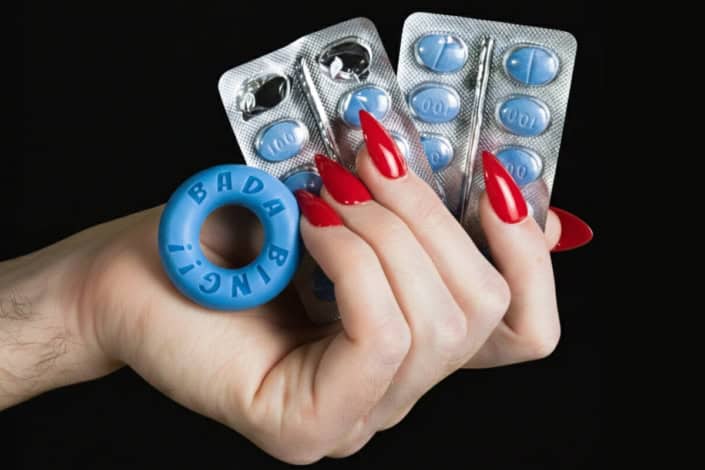 Mão segurando cartelas de viagra e um anel peniano